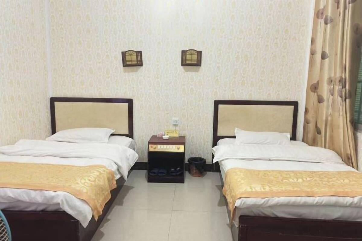 Quarto com duas camas, uma mesa de cabeceira com abajur e parede estampada.