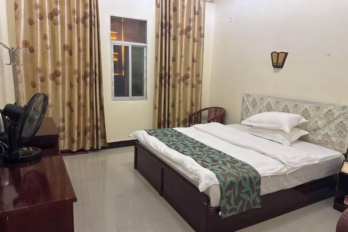 Um quarto com cama, escrivaninha, cadeira, janela e cortinas.