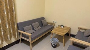Una sala pequeña con un sofá, una mesa de madera, un cubo de basura y una cortina.