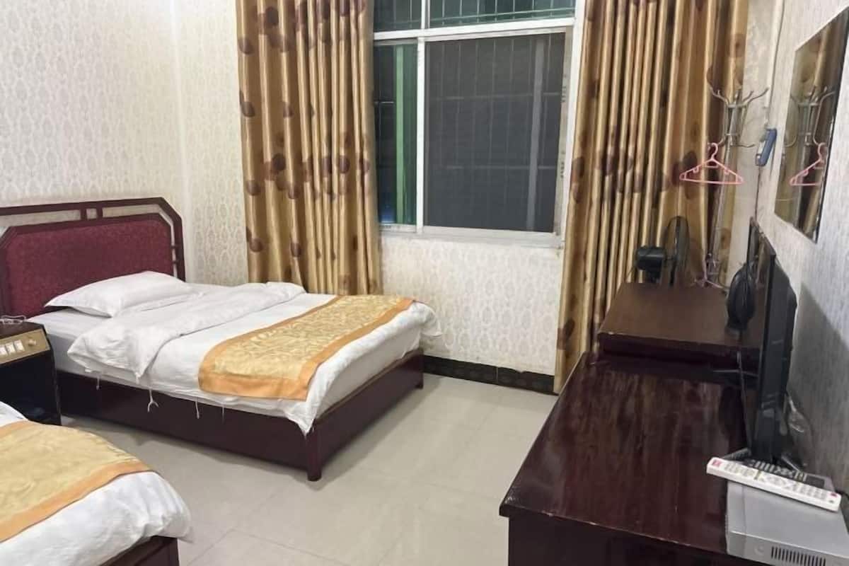 Quarto de hotel com duas camas, uma escrivaninha de madeira com televisão e uma janela com cortinas.