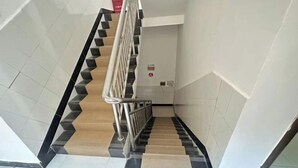 Una escalera con peldaños alternados en negro y color crema, paredes blancas y barandilla de metal.