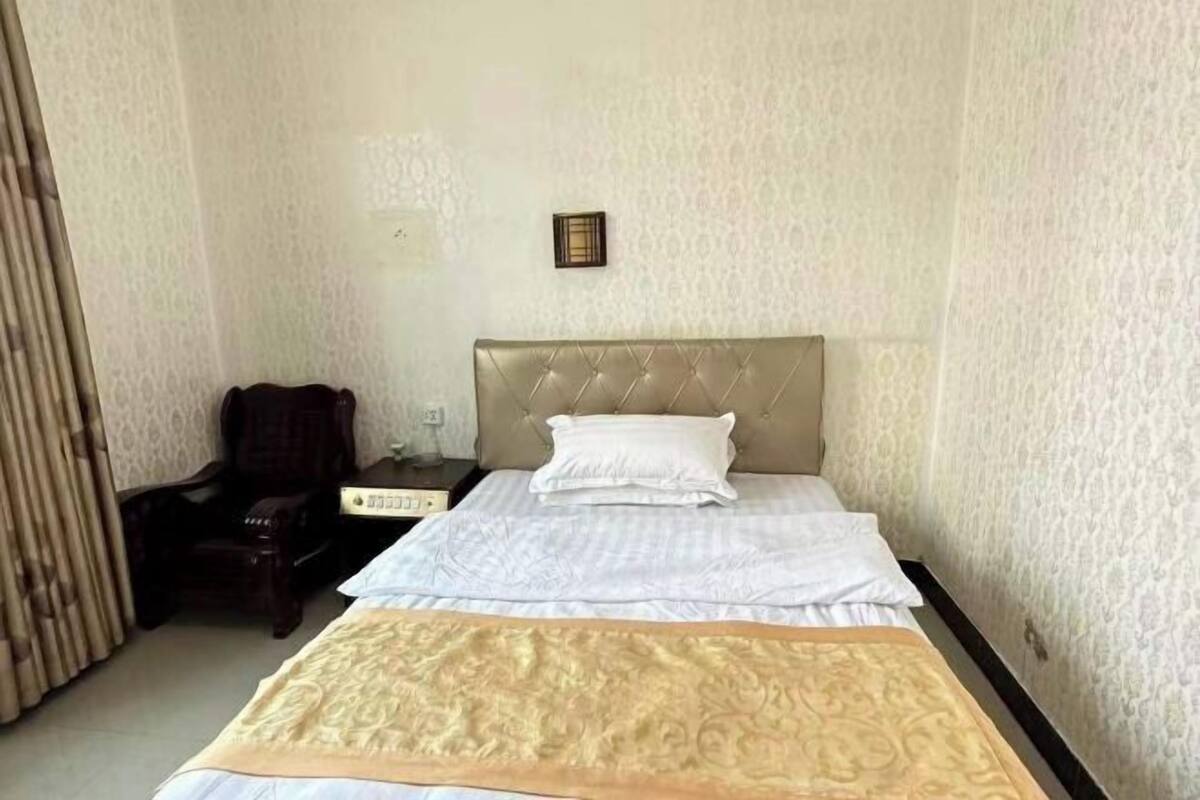 Quarto de hotel com cama, uma cadeira, mesa de cabeceira e luminária fixada na parede.