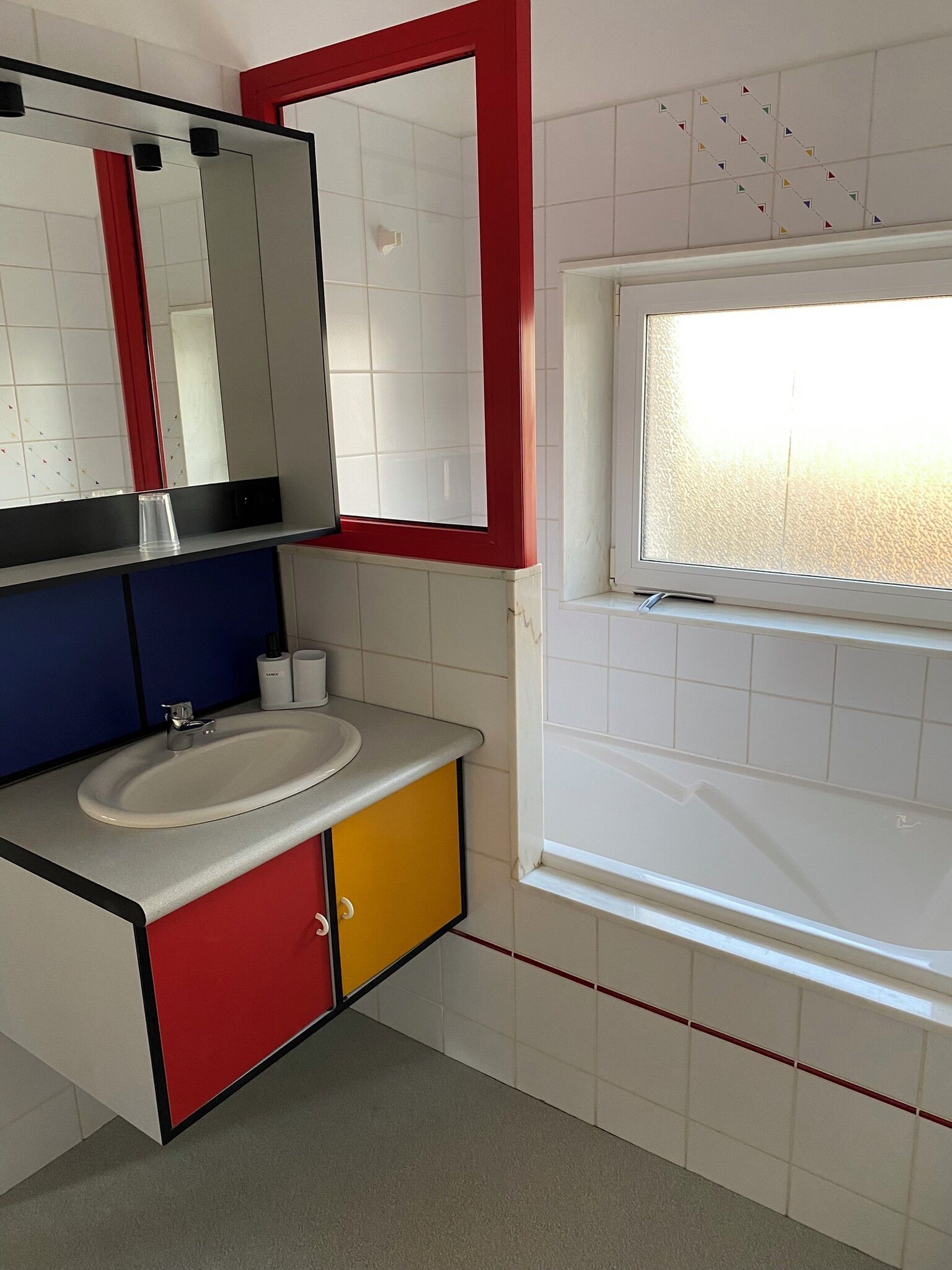 Une salle de bain avec un lavabo blanc, un miroir et une fenêtre.