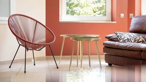 Ein modernes Wohnzimmer mit einem roten Sessel, einem kleinen runden Tisch und einem braunen Sofa mit einem gemusterten Kissen.