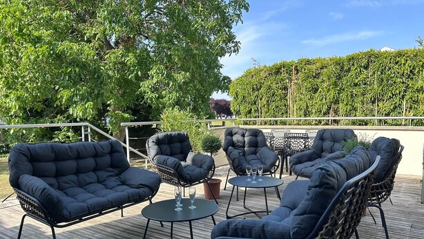 Ein Sitzbereich im Freien mit gepolsterten Stühlen und einem kleinen Tisch, umgeben von viel Grün und blauem Himmel.
