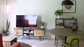 Ein modernes Wohnzimmer mit Fernseher, Holzmöbeln, einem Esstisch mit Stühlen und Pendelleuchten.