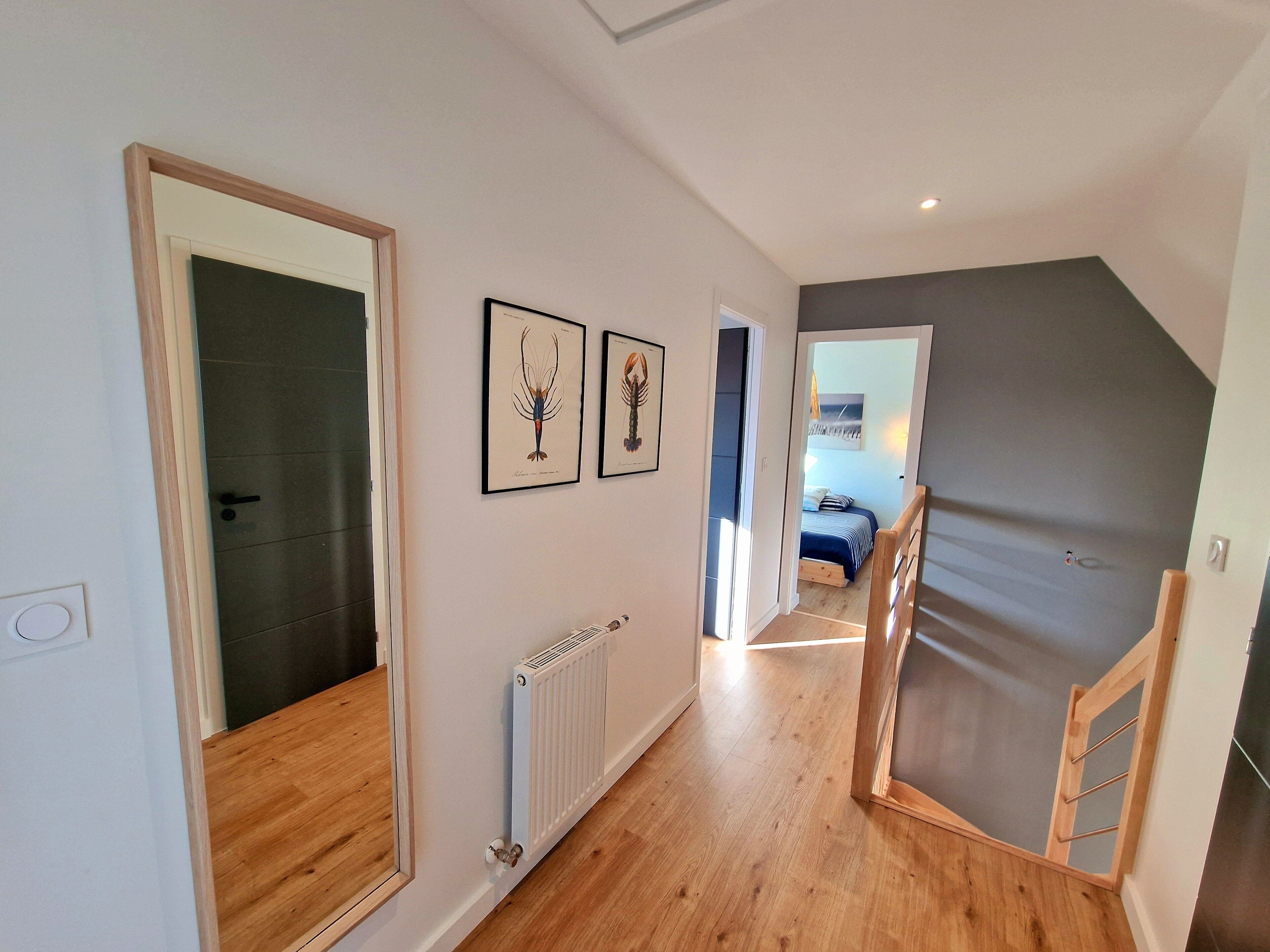 Un couloir doté d’un plancher en bois, d’un radiateur et de tableaux encadrés accrochés au mur.