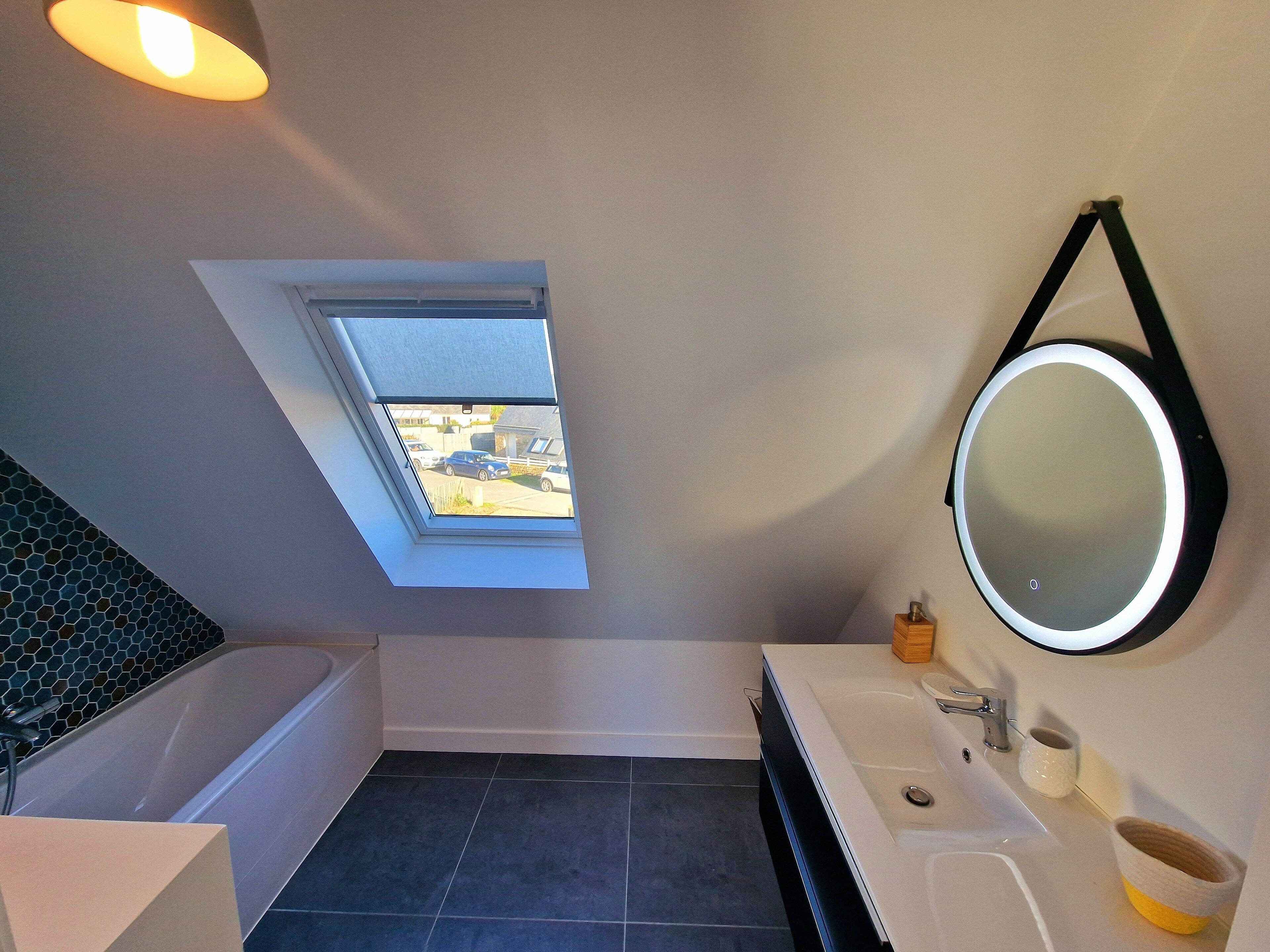 A modern bathroom with a skylight, a bathtub, a sink with a mirror, and a toilet.