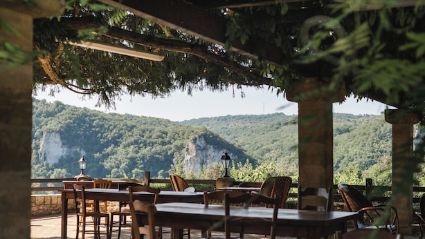 An outdoor dining area with tables and chairs, overlooking a forested mountain. - Domaine de Malet (Vitrac)