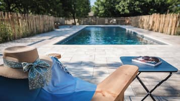 Zona de piscina con un banco de madera, un sombrero y un libro sobre una mesa.