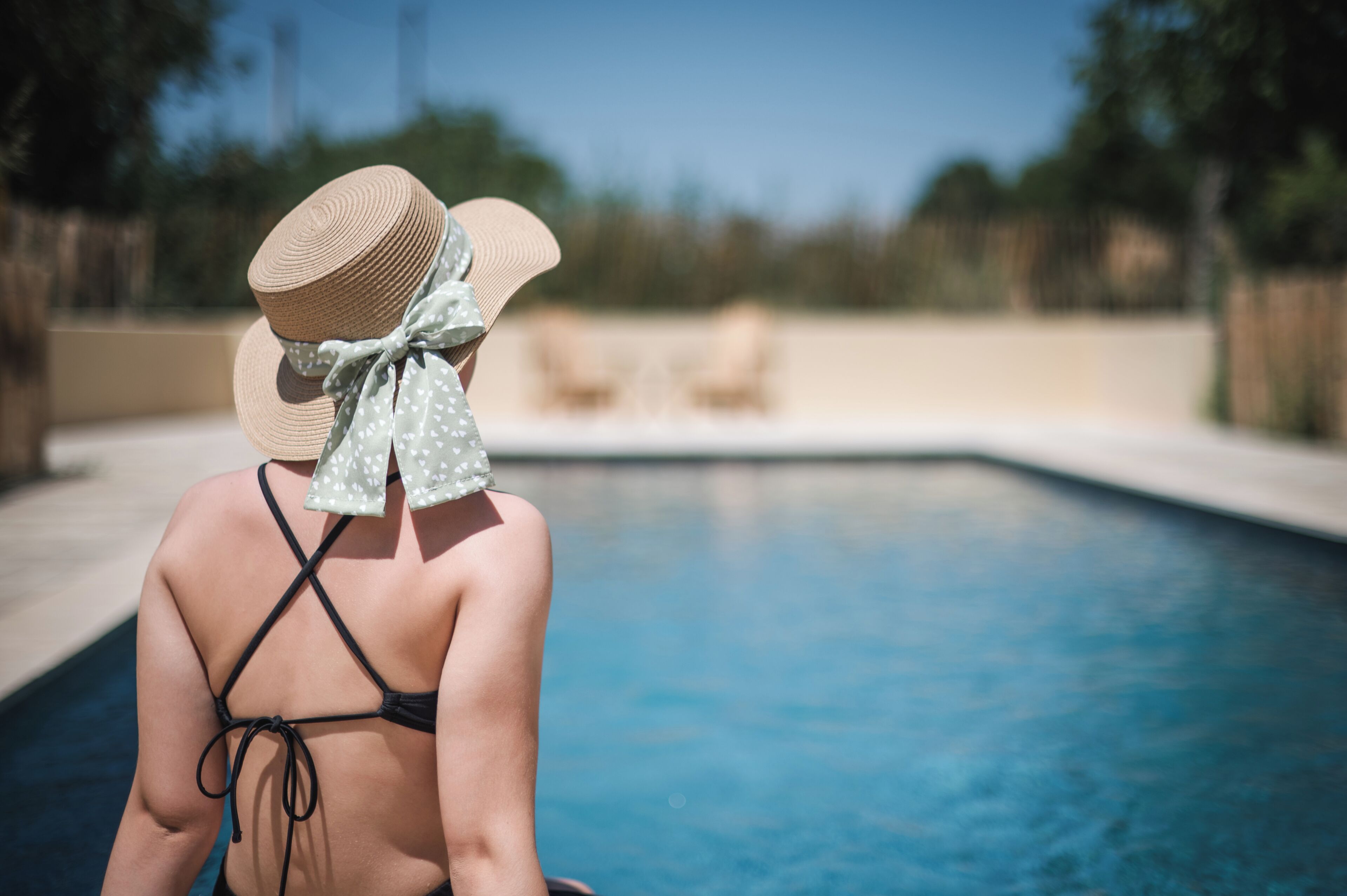 Una persona sentada junto a una piscina, con sombrero y un pañuelo de lunares al cuello.