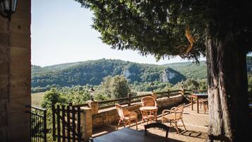 An outdoor patio with wicker furniture, stone railings, and a view of a forested hillside.