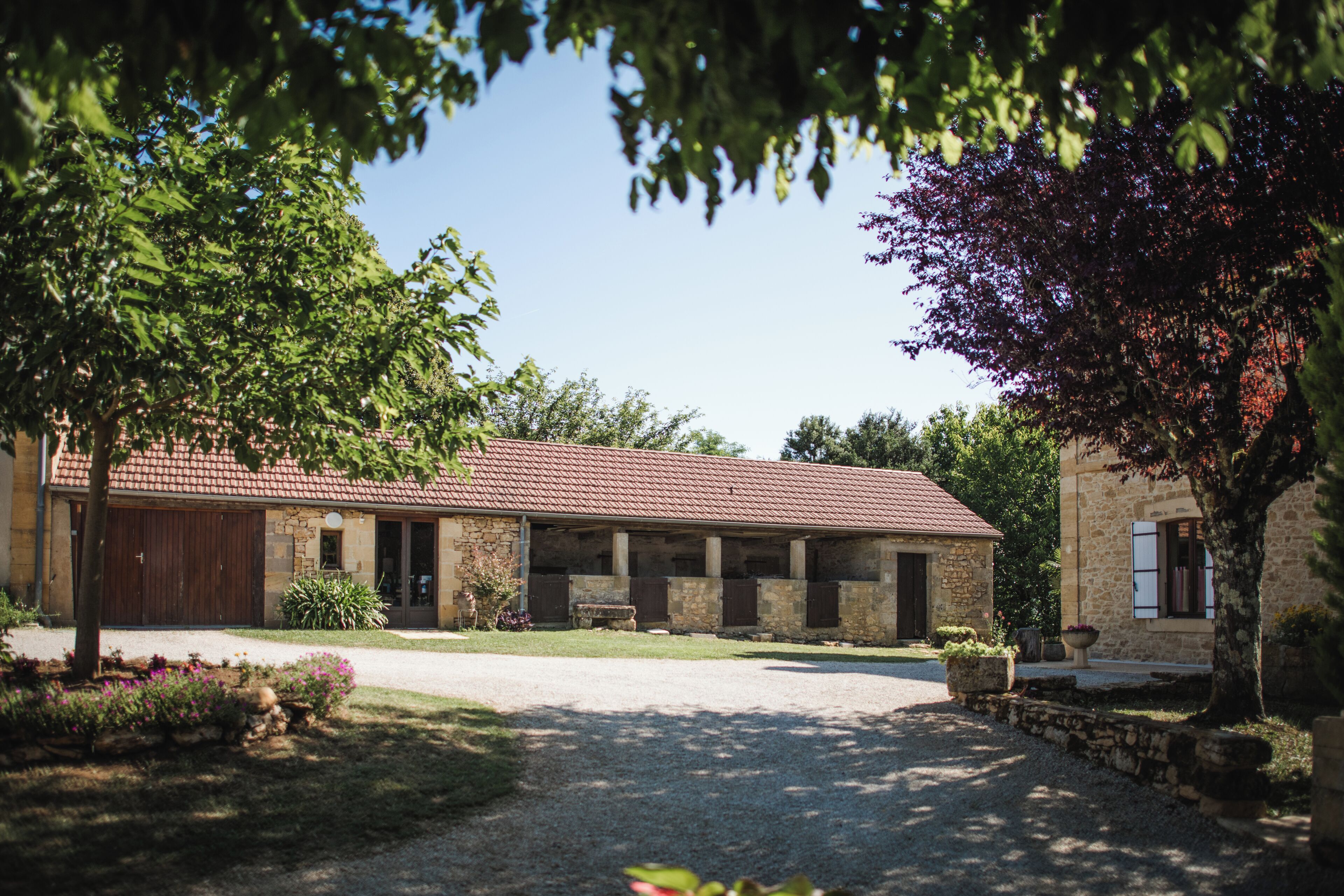A stone building with a red-tiled roof, a covered outdoor area, and a gravel driveway.