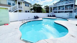 Une piscine au design incurvé, entourée d’une clôture blanche, et située à côté d’un immeuble à deux étages doté de balcons.