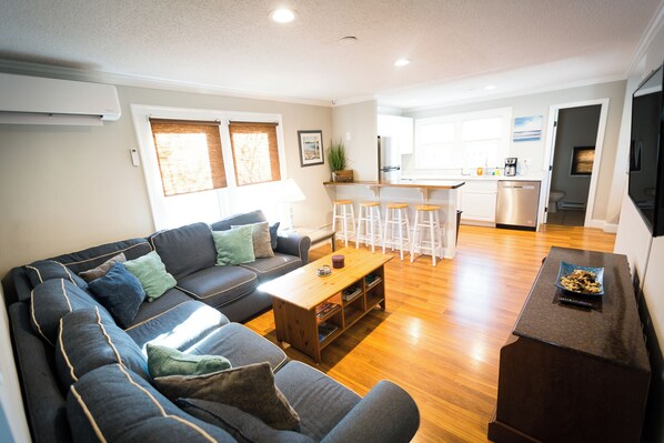 A modern living room with a sofa, coffee table, and a kitchen area in the background. - We provide Linens! 3-bedrooms, AC, WiFi, Pool in Downtown Ocean City (Ocean City)