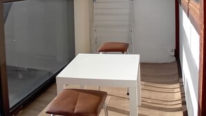Un balcón estrecho con una mesa blanca y dos sillas marrones.