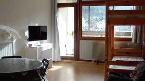 Una habitación con literas, una mesa de comedor con sillas, un televisor y una ventana con vistas a la nieve.