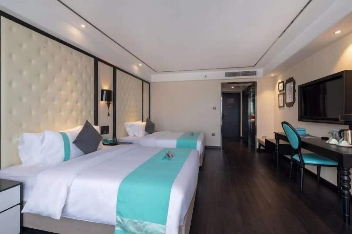A hotel room with two beds, a desk, a chair, and a large mirror.