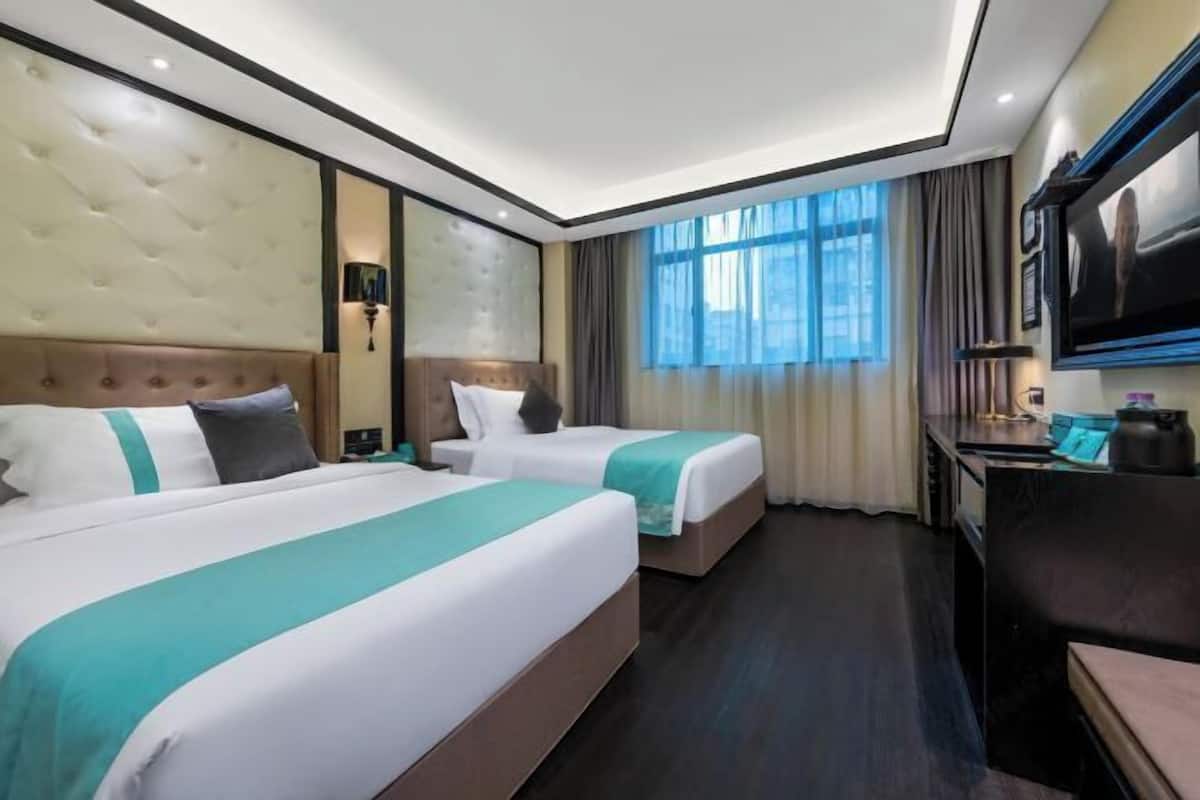 A hotel room with two beds, a desk, a TV, and a large window with curtains.