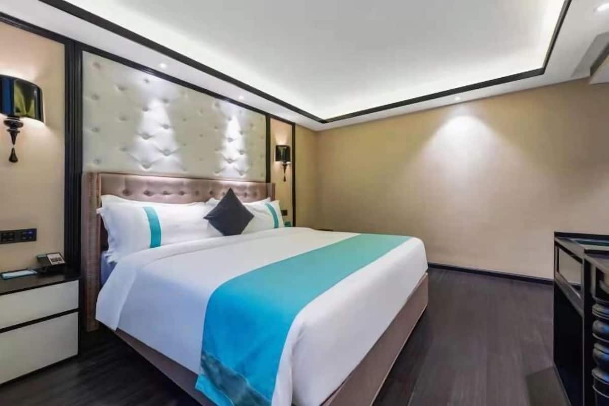 A hotel room with a large bed, a nightstand, a wall-mounted lamp, and a ceiling light.