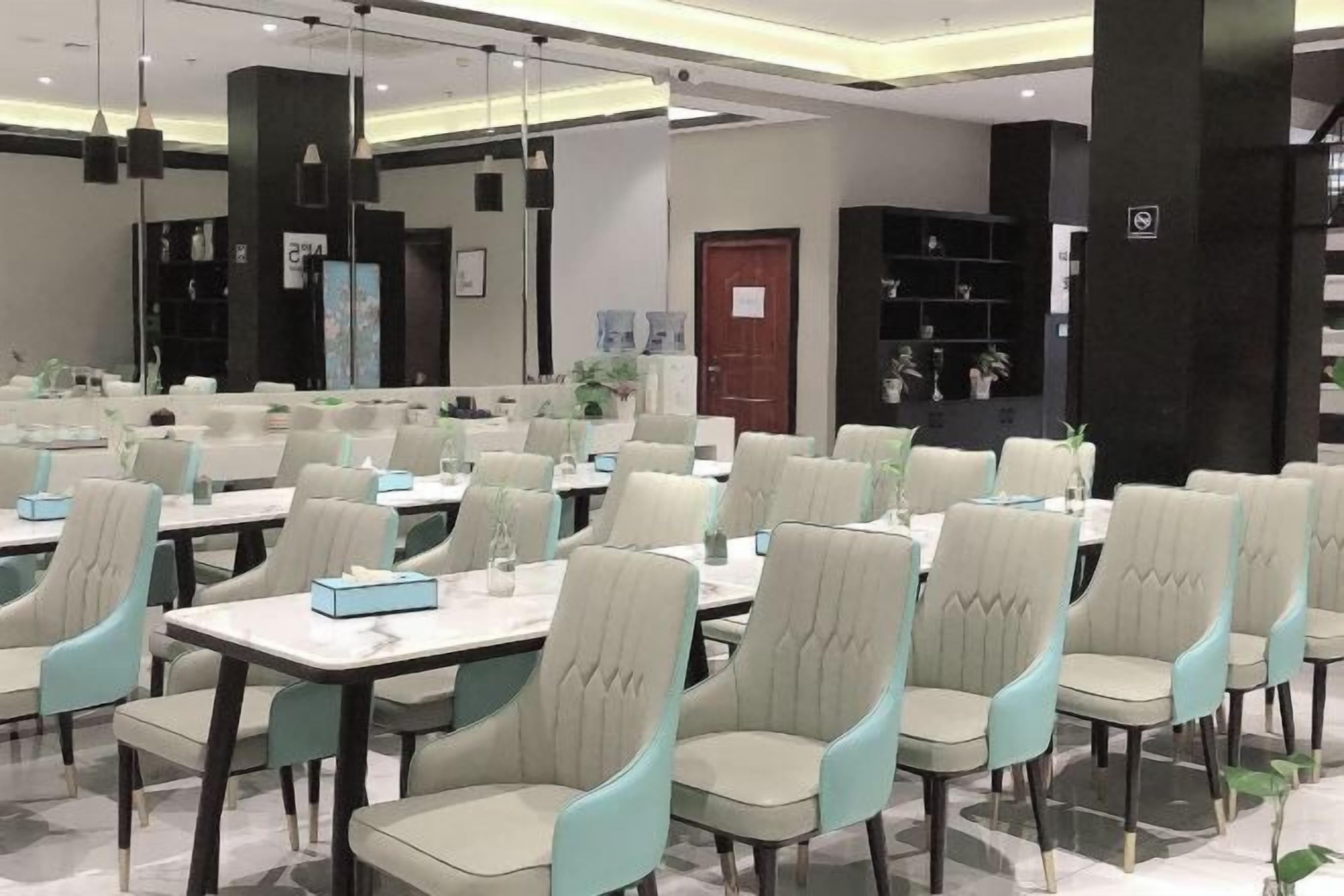 Un área de comedor moderna con varias mesas y sillas, una estantería negra y una puerta con un letrero.