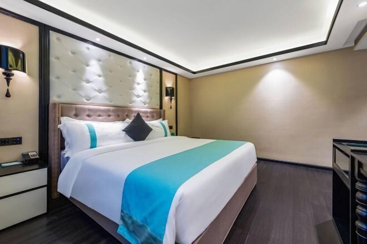 A hotel room with a large bed, a nightstand, a wall-mounted lamp, and a ceiling light.