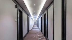 Un largo pasillo de hotel, estrecho, con piso alfombrado y una serie de puertas a un lado.