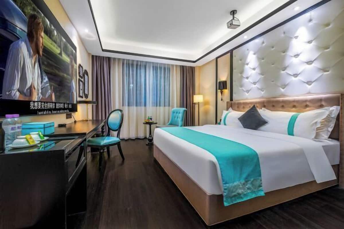 A hotel room with a large bed, a desk with a chair, a television, and a window with curtains.