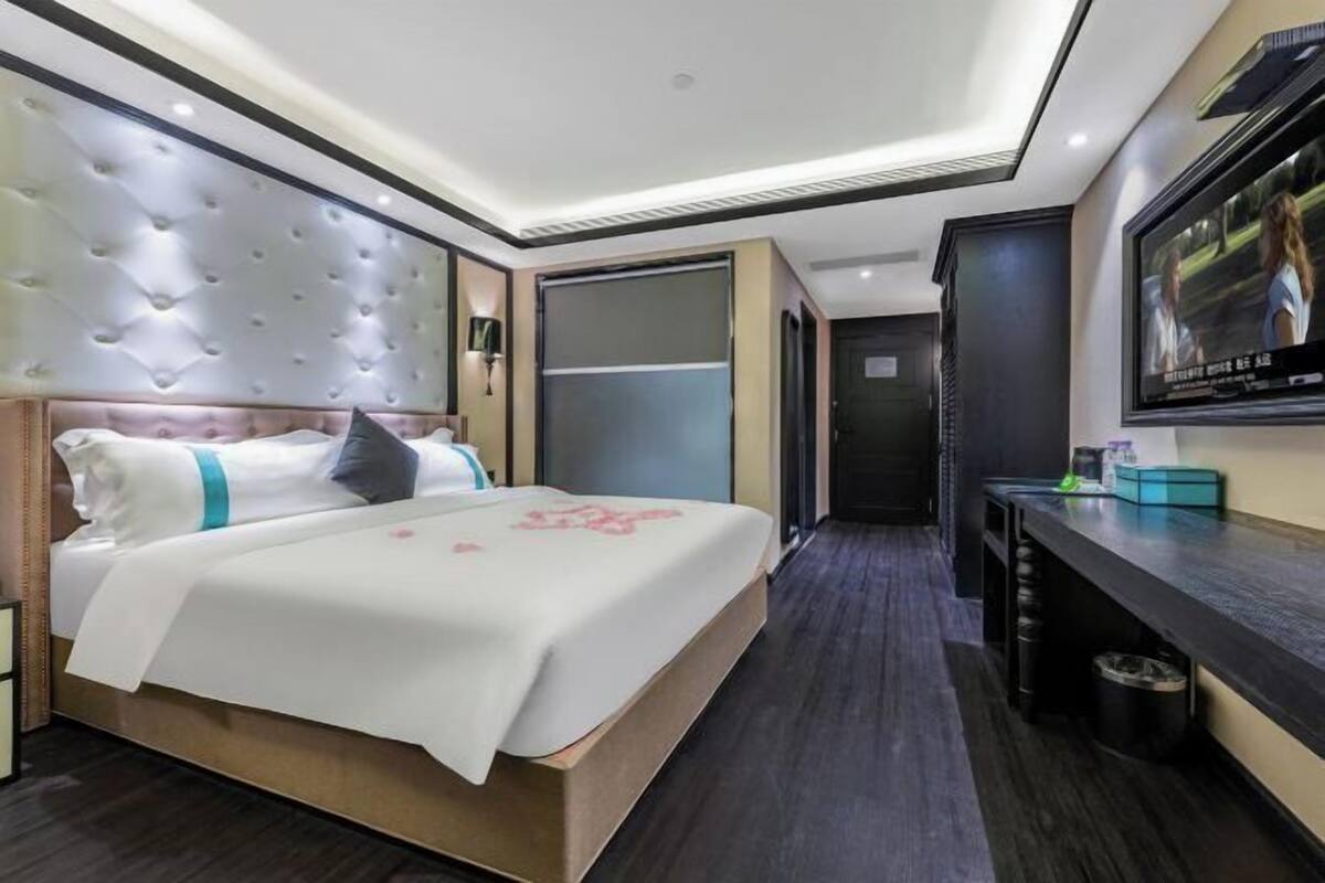 A modern hotel room with a large bed, a flat-screen TV, and a desk with a trash bin.