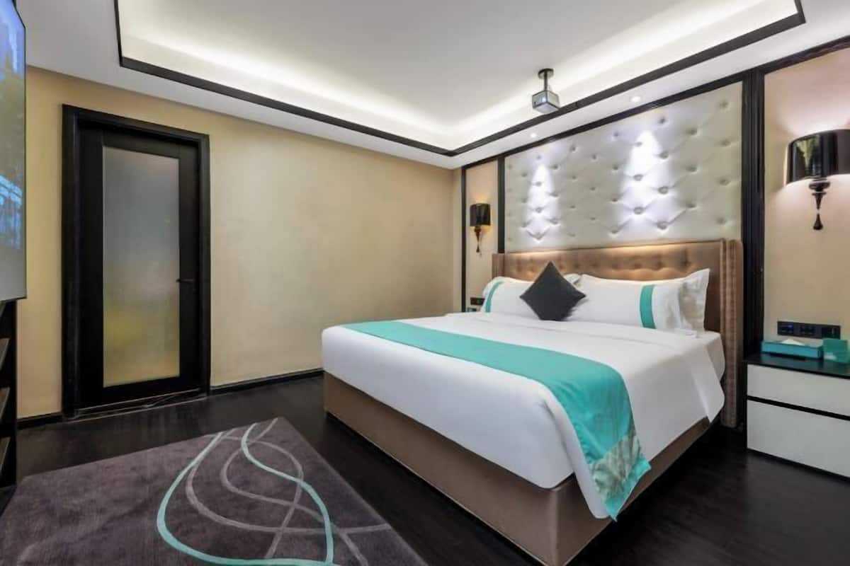 A modern hotel room with a large bed, a tufted headboard, a bedside table, and a nightstand.