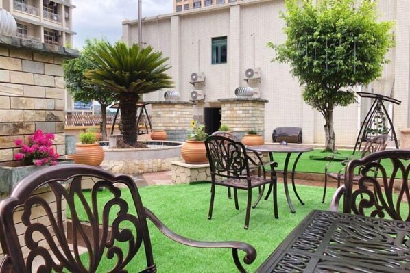 Un patio exterior con césped artificial, sillas y mesas de metal.