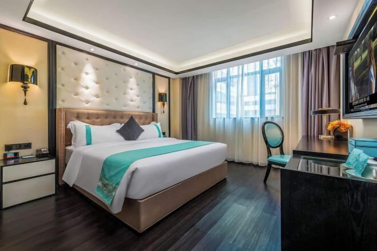 A hotel room with a large bed, a desk, a chair, a TV, and a window with curtains.