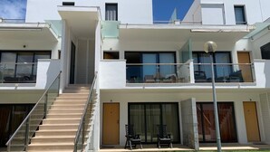 Ein modernes, mehrstöckiges Gebäude mit einer Treppe, die zu einem Balkon führt, großen Fenstern und einem gepflegten Rasen.