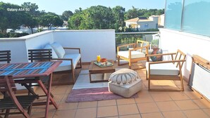Eine Dachterrasse mit einer Couch, Sesseln, einem Tisch und einem kleinen Hocker.