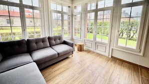 A spacious living room with a grey sectional sofa, large windows, and a wooden floor. - Charming house close to the beach and Mers les bains (Criel-sur-Mer)