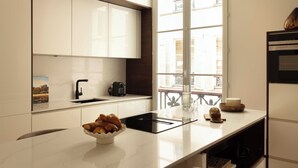 A modern kitchen with white cabinetry, a black countertop, and a window with a view of buildings. - Elegant Apartment - 2br- 6P- Gare Saint Lazare (Paris)