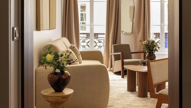 A living room with a sofa, a chair, a small table with a vase, and a view through a window with curtains. - Elegant Apartment - 2br- 6P- Gare Saint Lazare (Paris)
