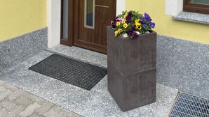 Une entrée d’immeuble avec une porte en bois, un jardinier et une enseigne indiquant « VIA AL FORTE 1 ».