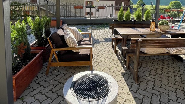 Une terrasse extérieure avec un banc en bois, un barbecue et des plantes en pot.