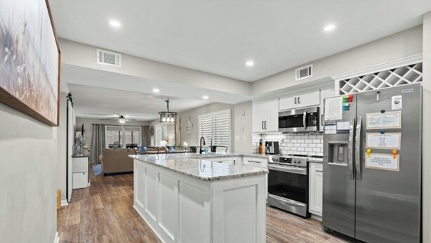 A modern kitchen with white cabinetry, a central island, stainless steel appliances, and a wooden floor. - Heron Pointe E8 - Golf, Beach, Pool, & Hot Tub (Myrtle Beach)