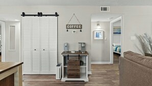 A living room with a coffee station, a white closet, and a couch. - Heron Pointe E8 - Golf, Beach, Pool, & Hot Tub (Myrtle Beach)