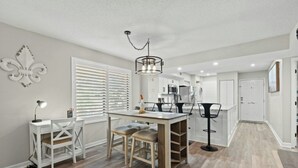A modern kitchen with a dining area, featuring a central island, pendant lighting, and a view into the adjacent living space. - Heron Pointe E8 - Golf, Beach, Pool, & Hot Tub (Myrtle Beach)