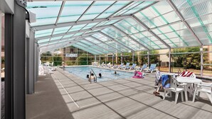 An indoor swimming pool with clear glass ceilings, lounge chairs, and a concrete floor. - Heron Pointe E8 - Golf, Beach, Pool, & Hot Tub (Myrtle Beach)