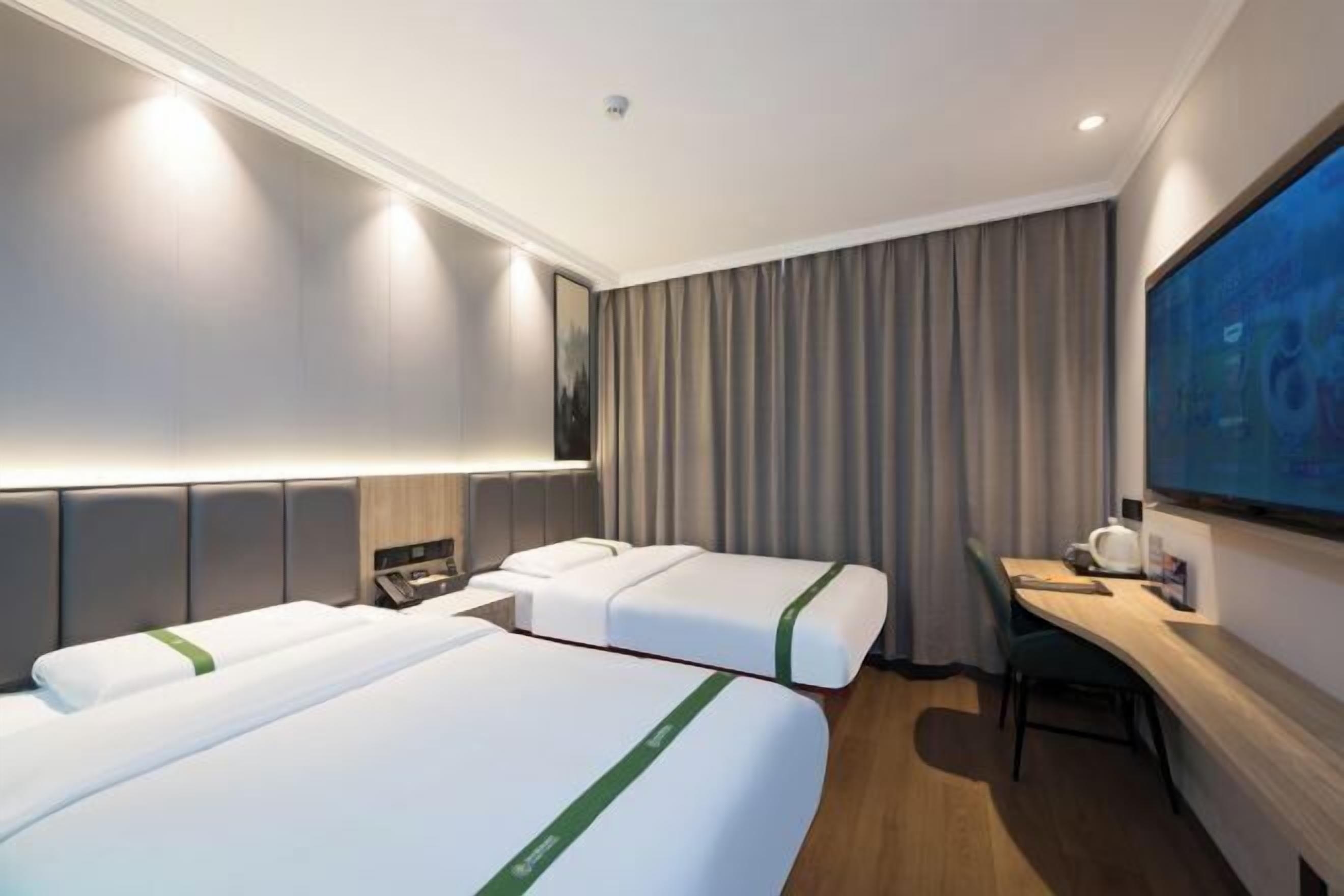 Une chambre d’hôtel avec deux lits, un bureau, une chaise, un téléviseur à écran plat et une grande fenêtre avec des rideaux.