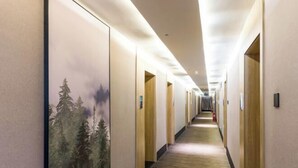 Passadís d'hotel amb sòl de fusta, portes a banda i banda i un cartell gran amb una escena de bosc a la paret esquerra.