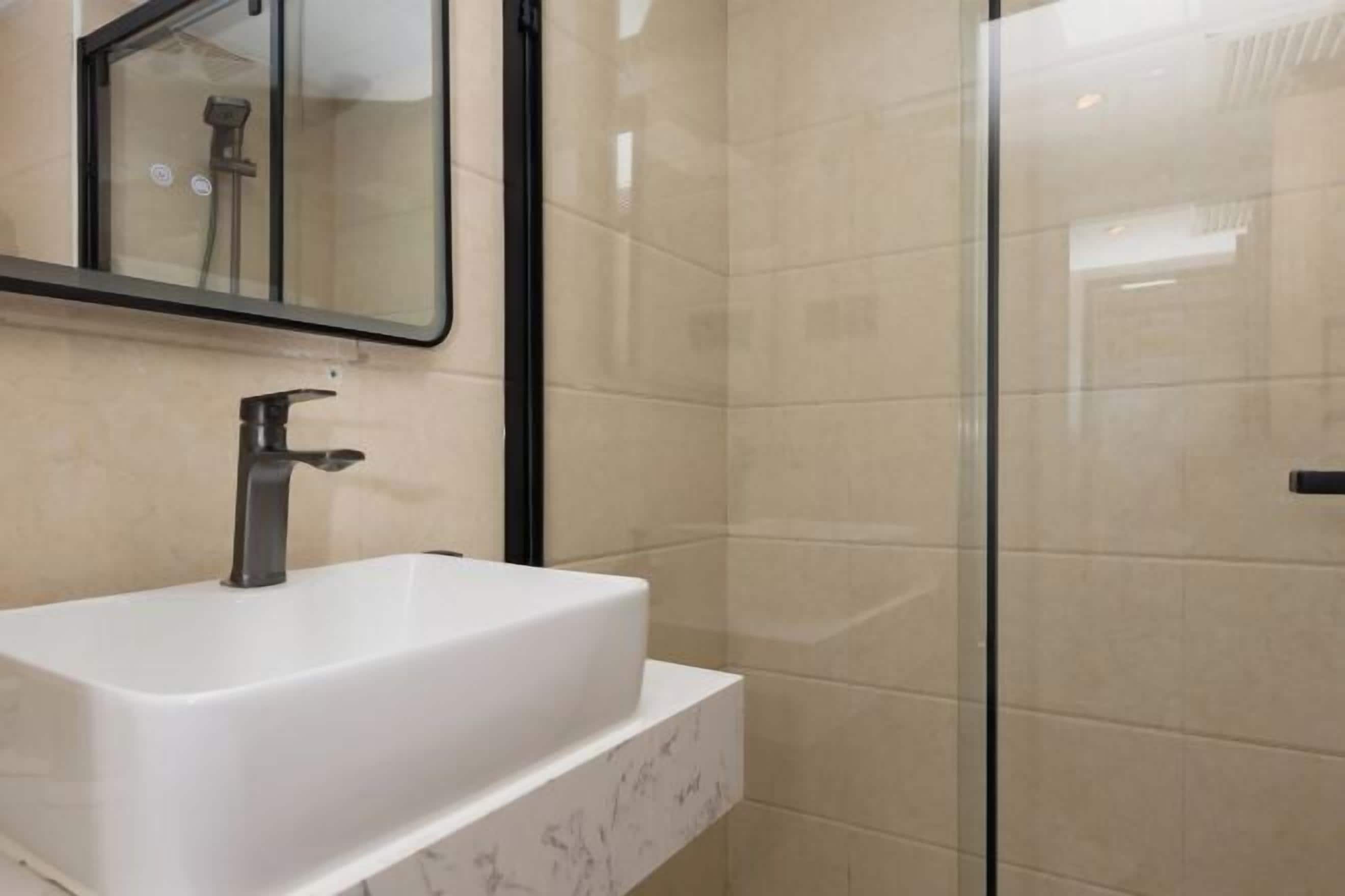 A modern bathroom with a white sink, a mirror, and a glass shower enclosure.