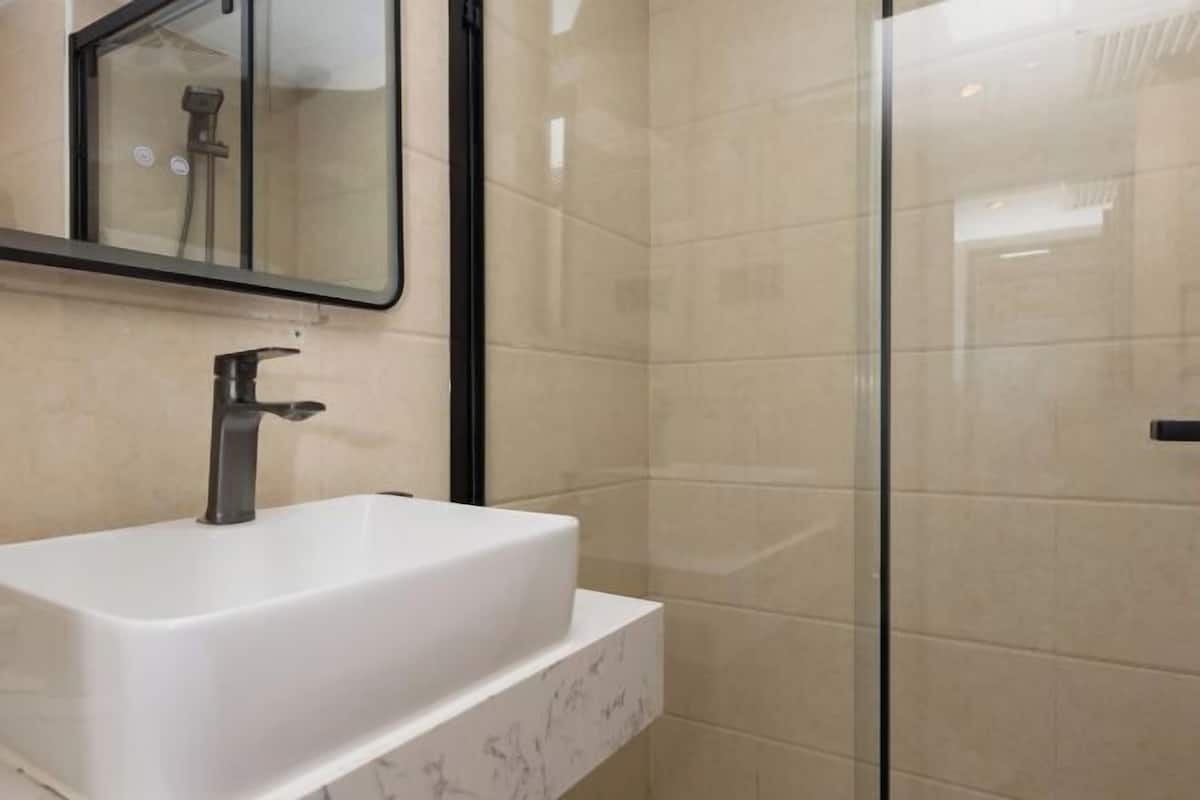 A modern bathroom with a white sink, a mirror, and a glass shower enclosure.