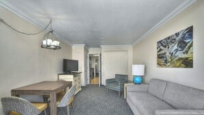 A hotel room with a wooden dining table, a gray sofa, a television, and a painting on the wall. - Coral Beach 1022-Oceanfront 1BR-Pools-Lazy River (Myrtle Beach)