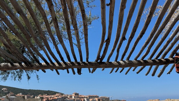 Vista costera con una pérgola de madera, un banco de piedra y una mesa redonda de madera.