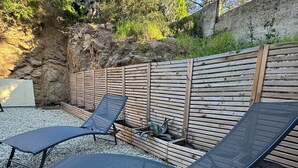 Dos sillones de sala con estructura metálica y cojines oscuros, ubicados sobre una superficie de grava con una valla de madera y follaje al fondo.